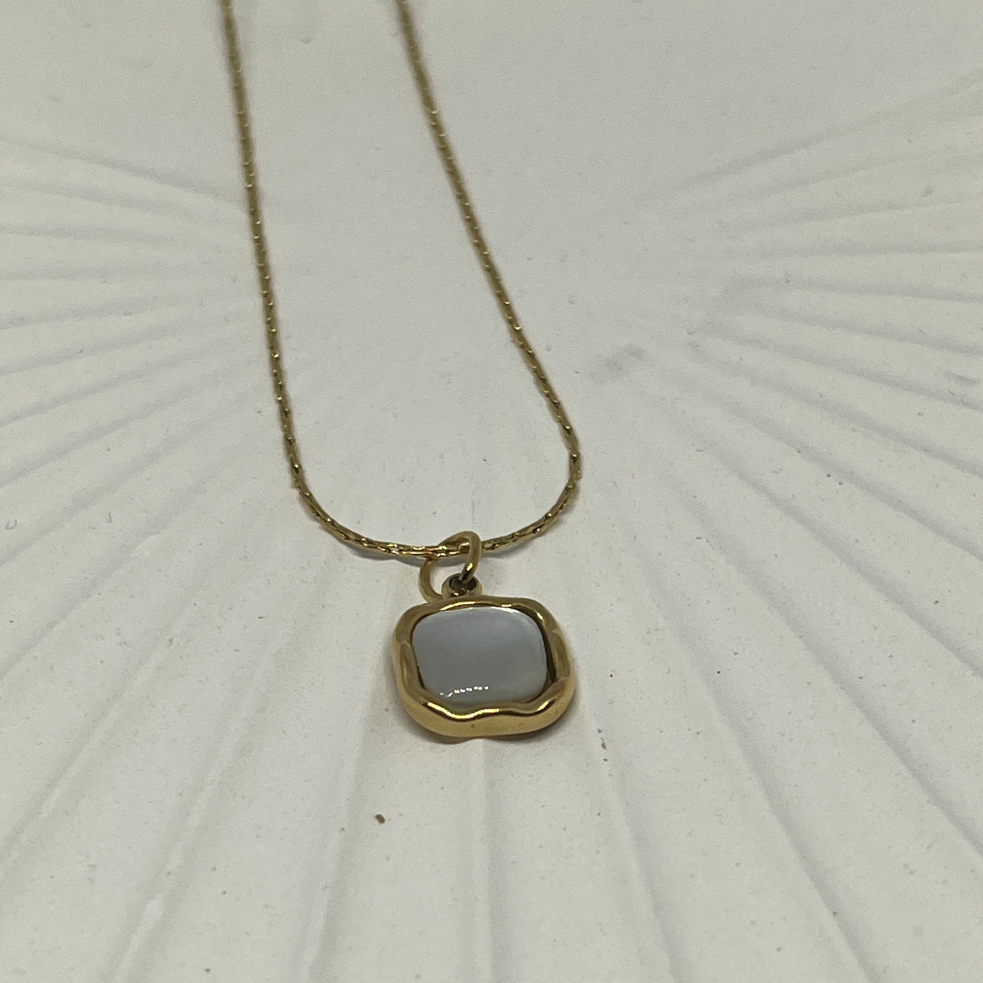 Gold necklace with a pendant on a textured white surface