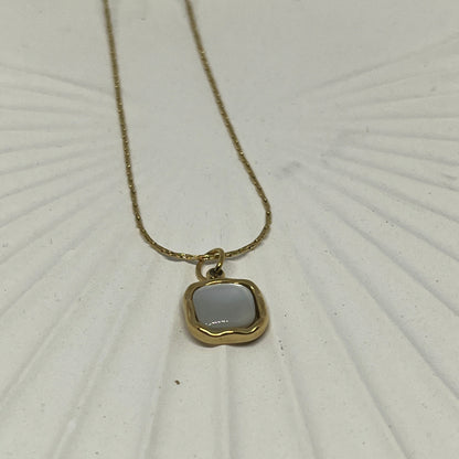 Gold necklace with a pendant on a textured white surface